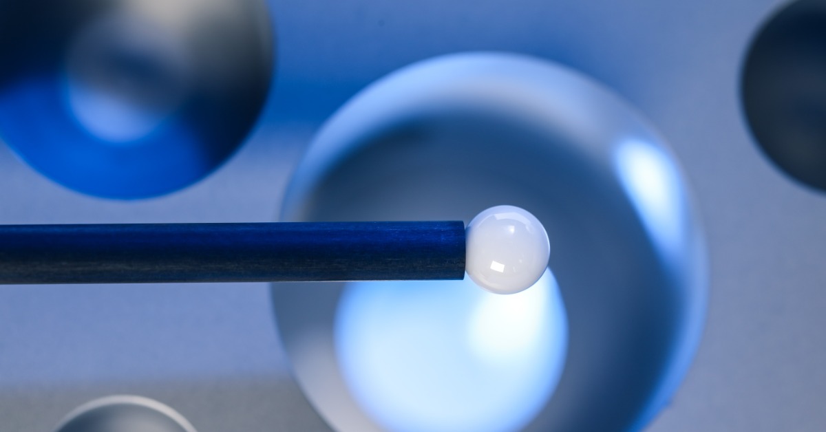 A close-up of a white stylus ball on a black probe stem. Soft light highlights its glossy surface.